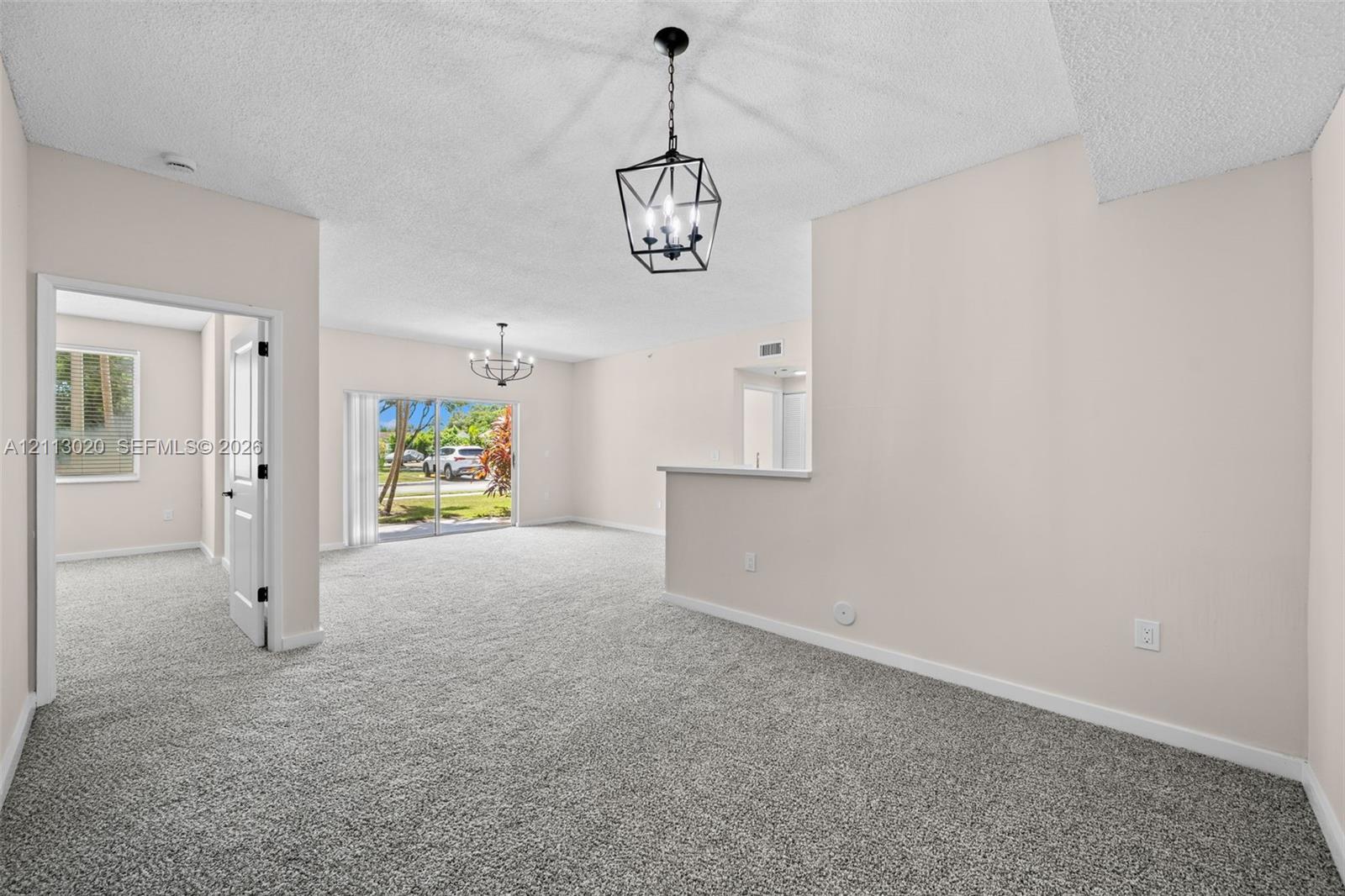 Interior space featuring neutral-toned carpeting, geometric metal chandeliers, glass sliding doors, and a partial partition wall