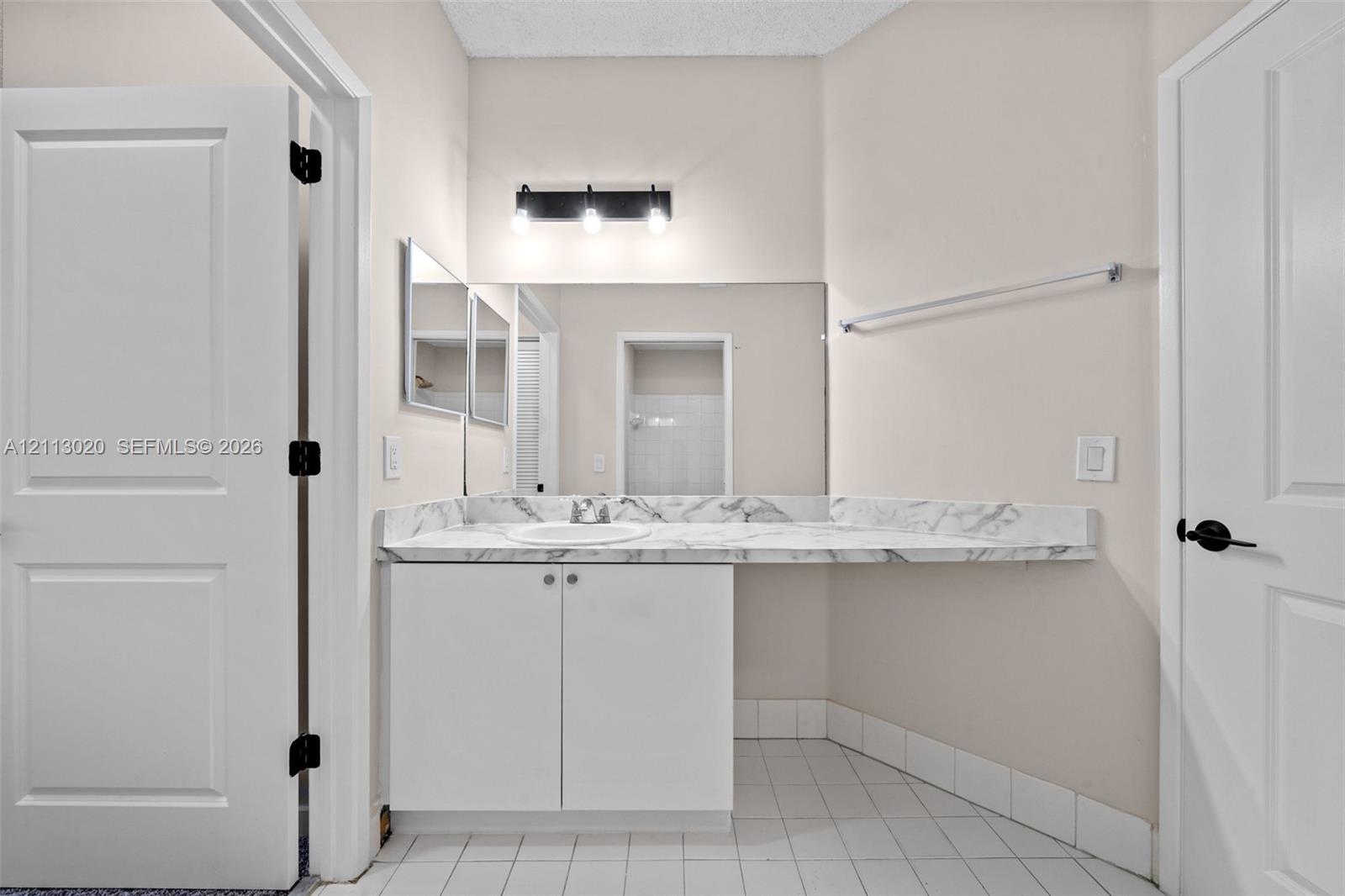 Bathroom vanity featuring stone-patterned countertop with integrated sink, white cabinetry, wall-to-wall mirror, three-light fixture, and ceramic tile flooring
