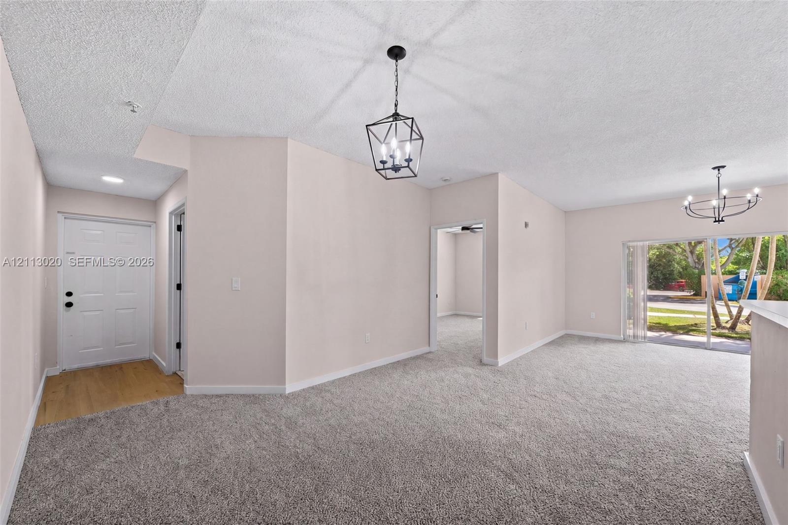 Interior space featuring neutral wall tones, wall-to-wall carpeting, metal geometric pendant lighting, and sliding glass doors with exterior access
