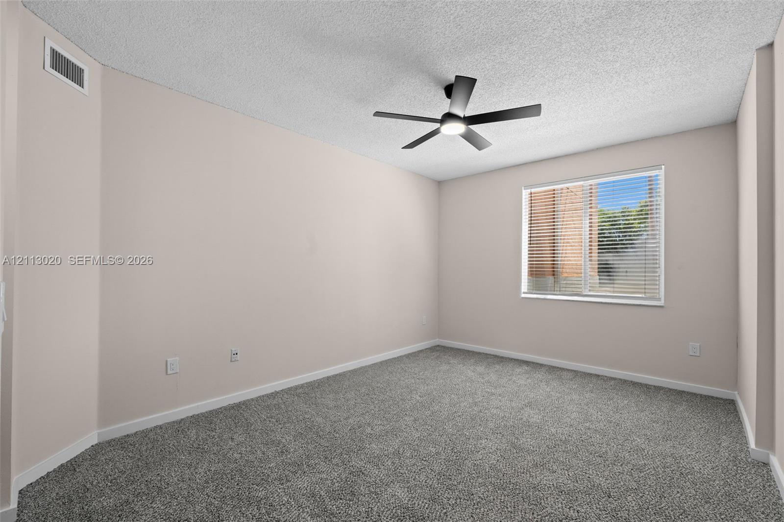 Room featuring neutral wall tones, gray carpeting, a textured ceiling, and a ceiling-mounted light fixture with a fan