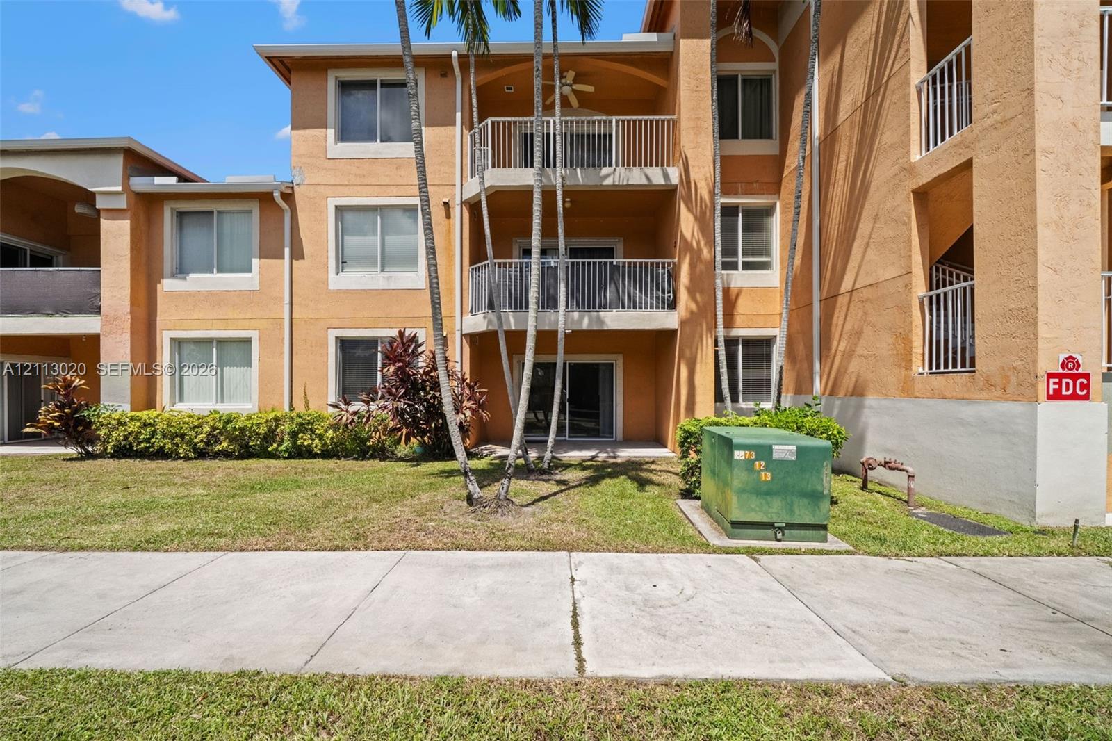 Stucco exterior featuring multi-level balconies with metal railings, sliding glass doors, and manicured landscaping