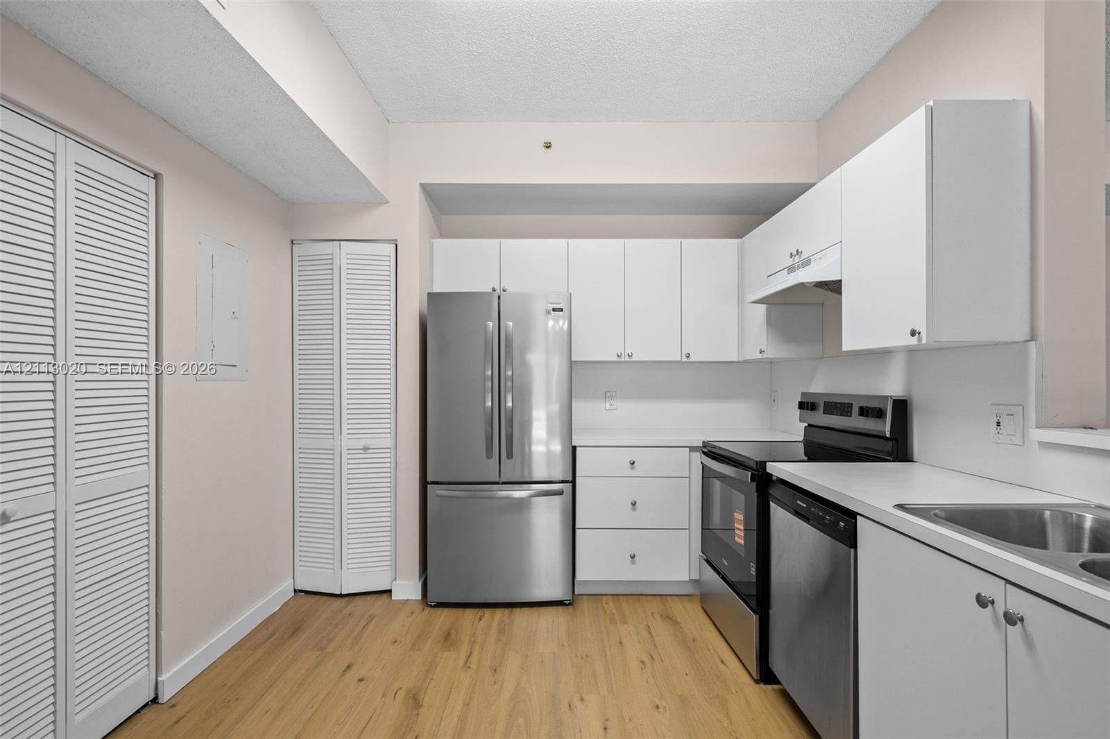 Kitchen featuring white cabinetry, stainless steel appliances, solid-surface countertops, wood-finish flooring, and louvered-style closet doors