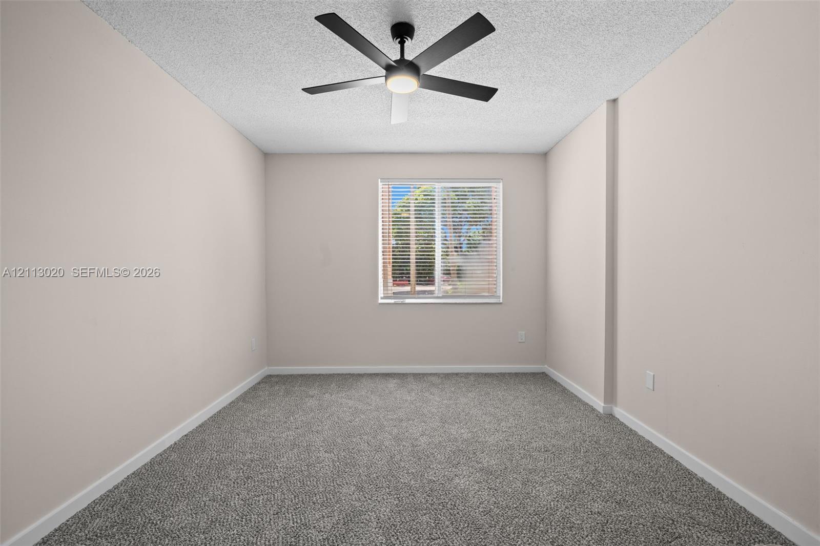 Neutral-toned interior space featuring neutral wall-to-wall carpeting, a centered matte black ceiling fan with integrated lighting, and a single window with horizontal blinds