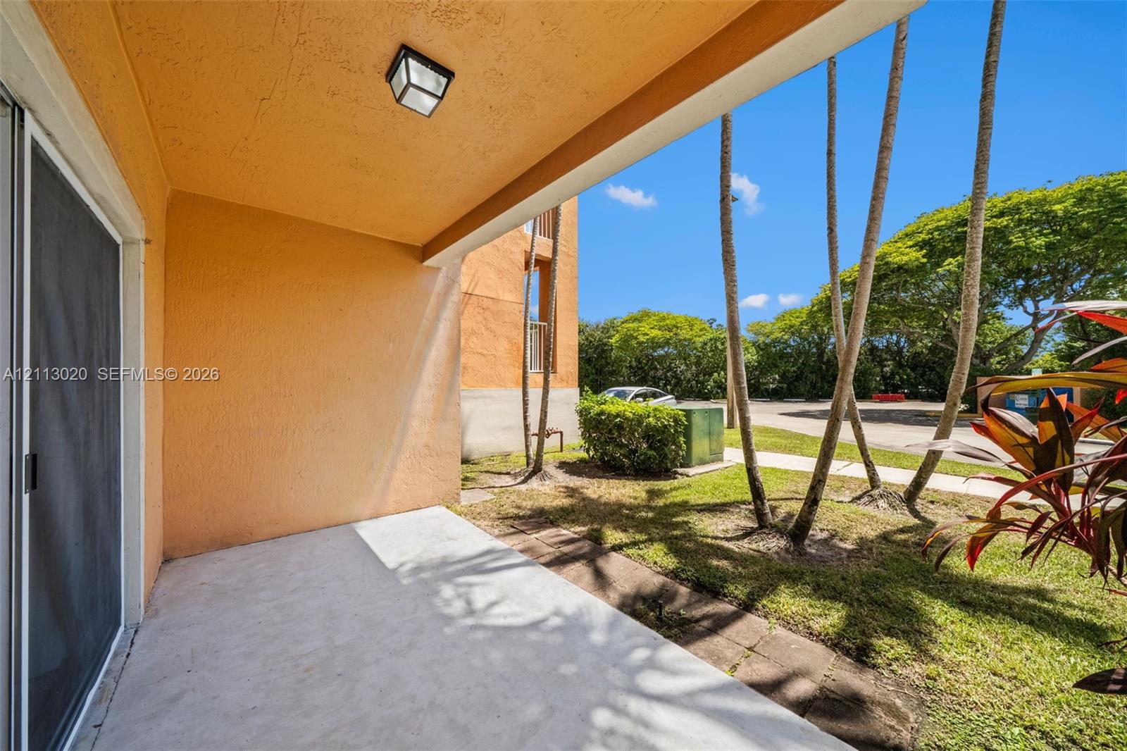 Covered ground-level patio with concrete flooring, stucco exterior wall, and wall-mounted light fixture