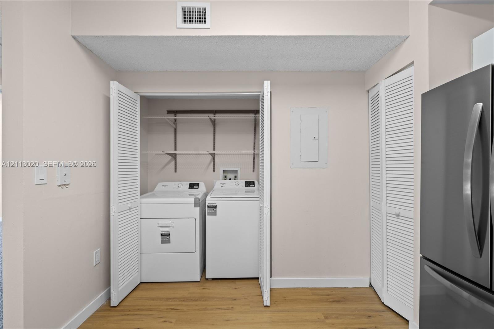 Laundry area featuring white bi-fold louvered closet doors, adjustable wire shelving, and wood-finish flooring