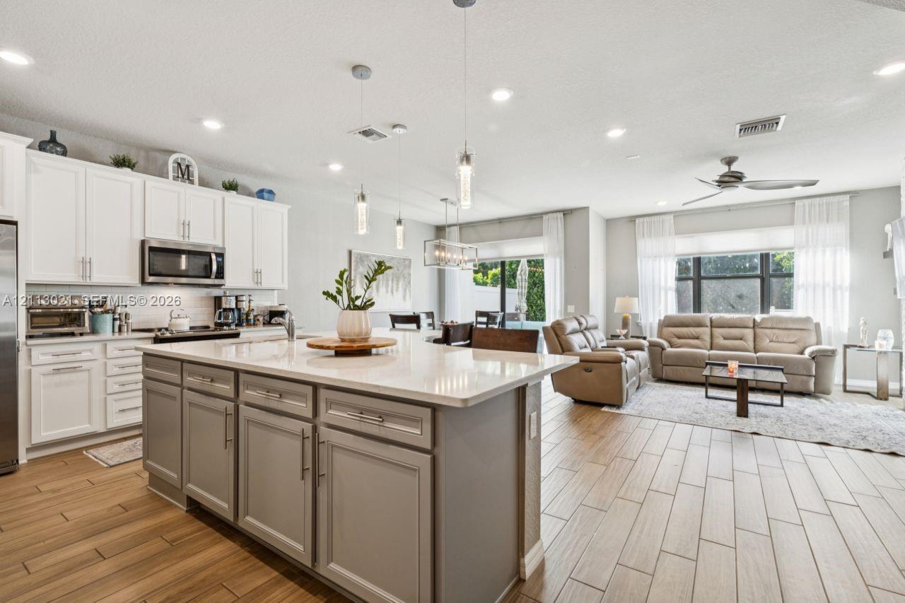 Kitchen featuring an expansive center island with stone-finish countertops, ceiling-mounted pendant lighting, shaker-style cabinetry, and wood-finish flooring Kitchen featuring an expansive center island with stone-finish countertops, ceiling-mounted pendant lighting, shaker-style cabinetry, and wood-finish flooring