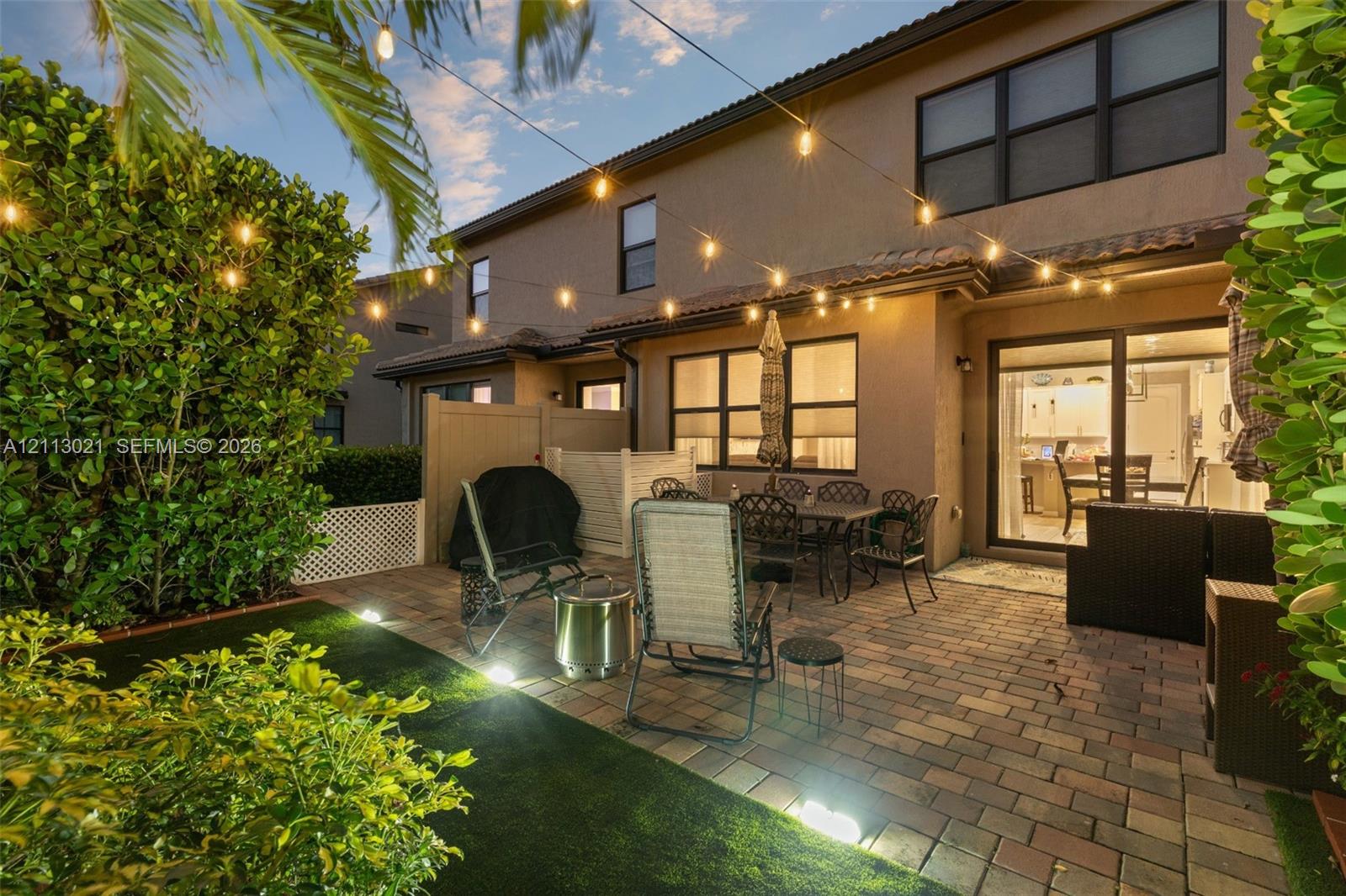 Paver patio featuring integrated landscape lighting, artificial turf, and privacy fencing