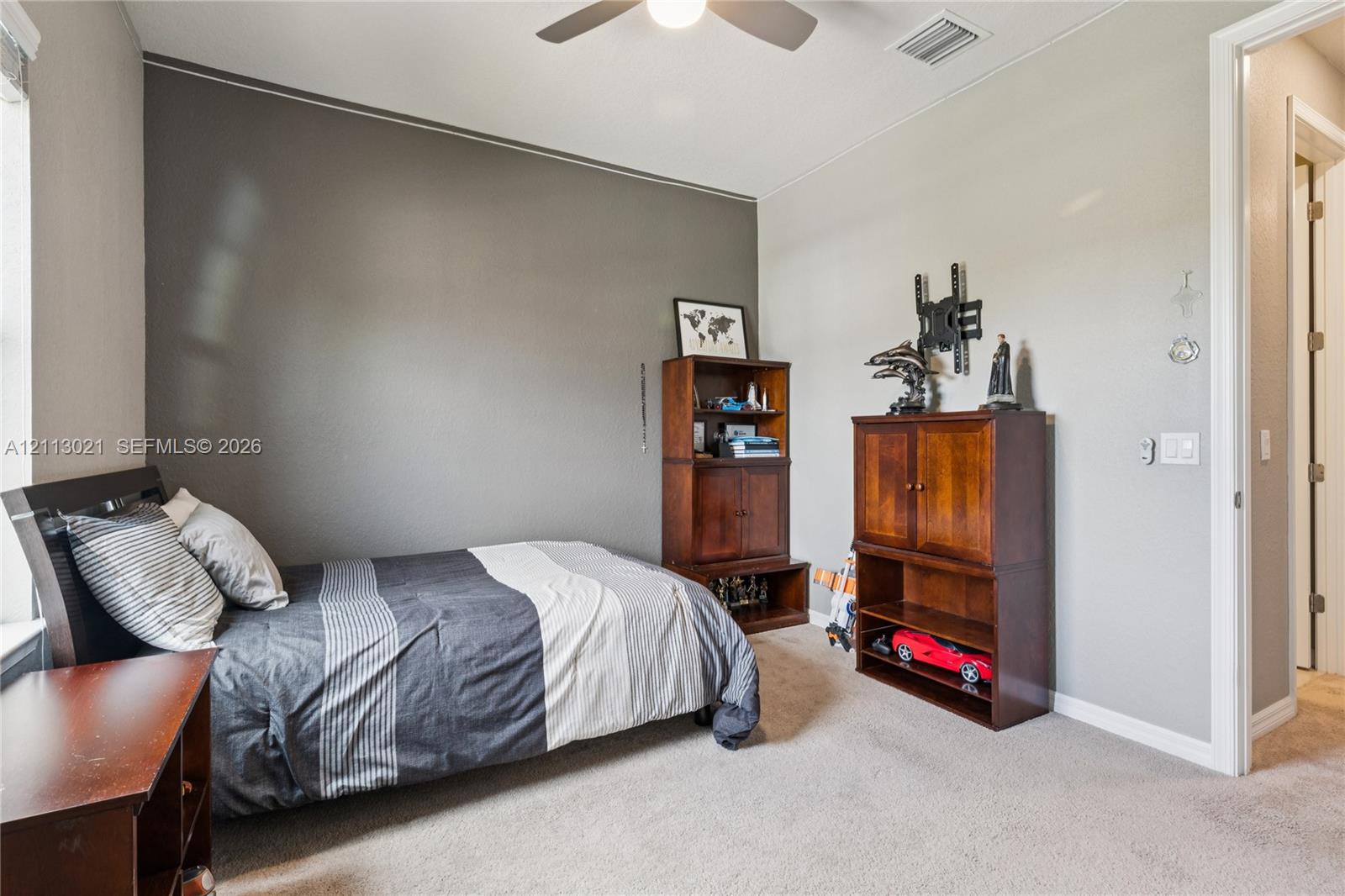 Interior room featuring a neutral color palette, charcoal accent wall, neutral carpeting, and a ceiling-mounted fan with light fixture