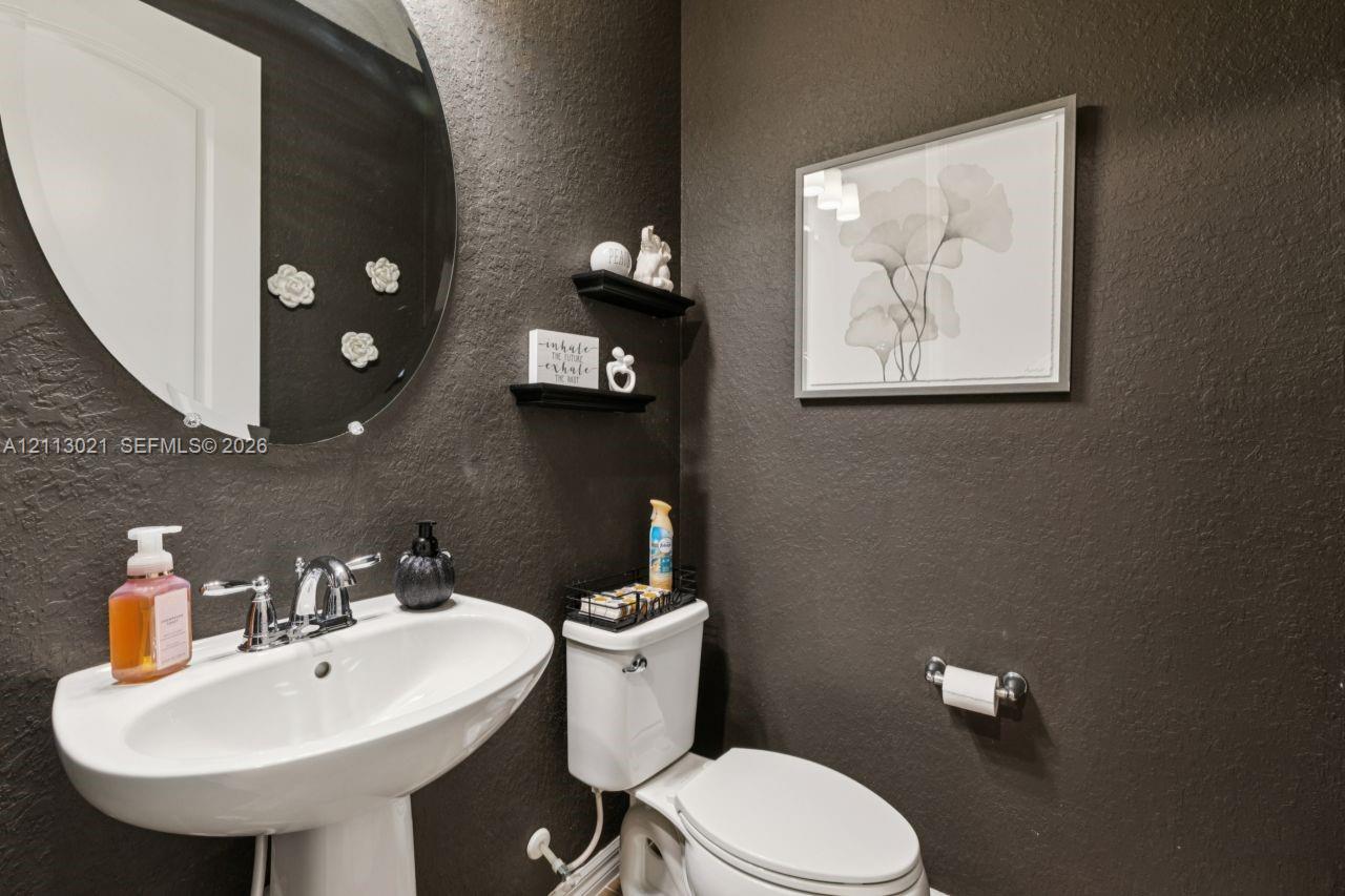 Oval wall-mounted mirror, white ceramic pedestal sink, chrome finish faucet, two built-in floating shelves, and textured dark-toned walls