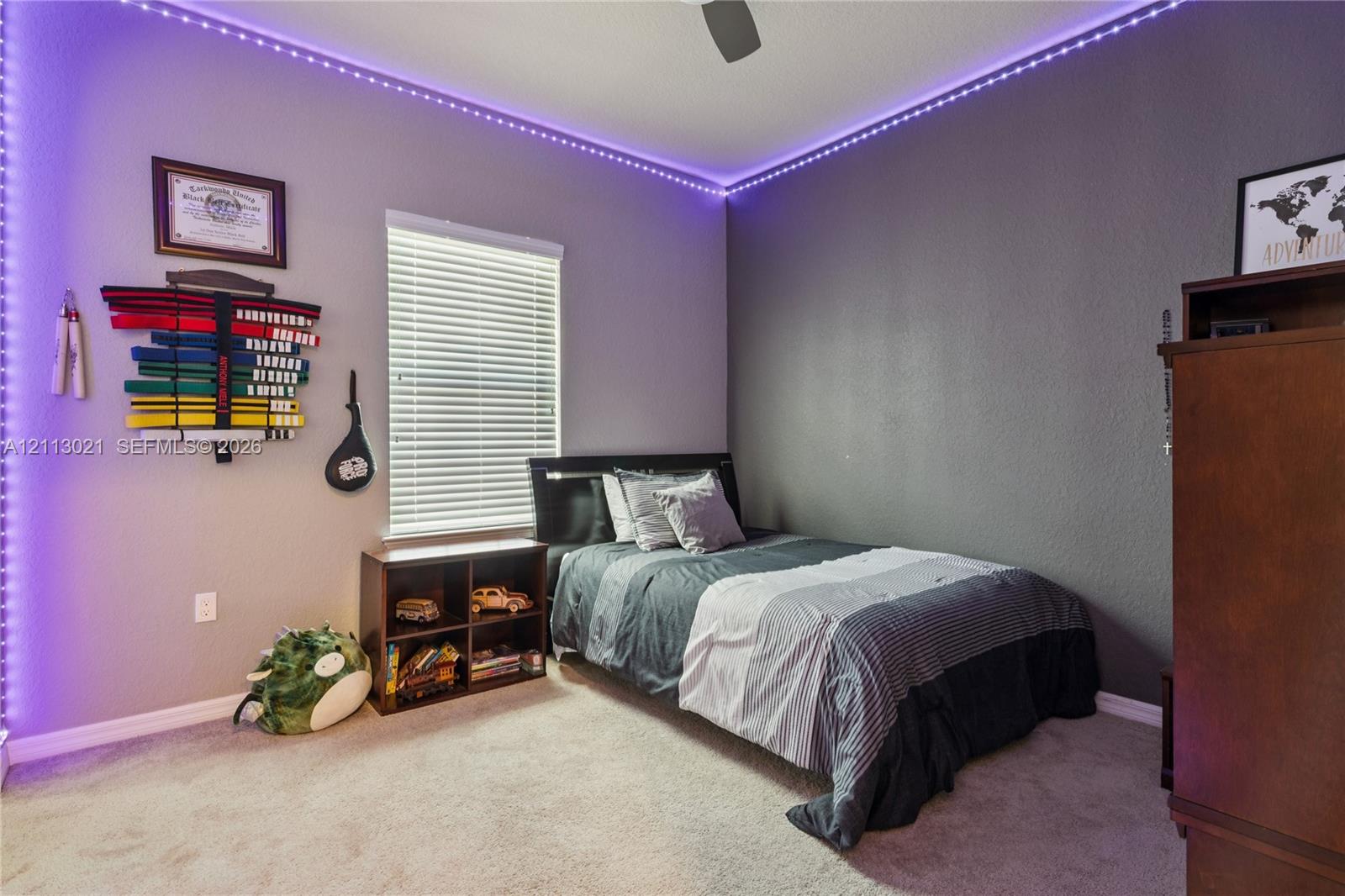 Bedroom featuring neutral carpeting, textured wall finish, integrated ceiling fan, and window with horizontal blinds