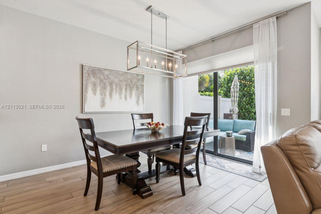 Dining area featuring wood-finish tile flooring, a rectangular metal-frame chandelier, and sliding glass doors leading to a paved patio