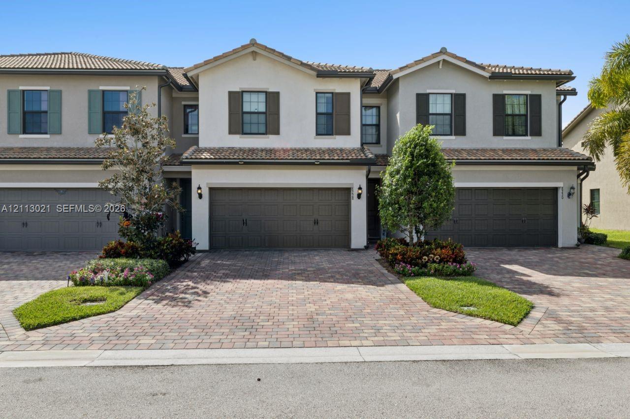 Multi-story exterior featuring a neutral stucco facade, decorative shutters, tile roofing, and brick-paver driveways with integrated landscaping