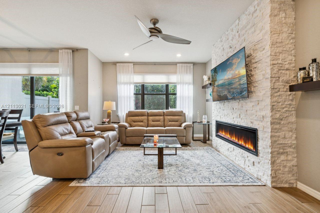 Living area featuring wood-finish tile flooring, recessed lighting, ceiling fan, and a floor-to-ceiling stone-veneer accent wall with an integrated linear electric fireplace