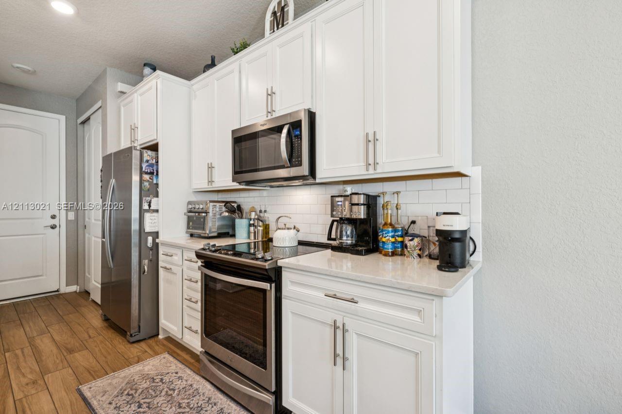 Kitchen featuring white Shaker-style cabinetry, stainless steel appliances, quartz countertops, and a white subway tile backsplash, complemented by wood-finish flooring Kitchen featuring white Shaker-style cabinetry, stainless steel appliances, quartz countertops, and a white subway tile backsplash, complemented by wood-finish flooring