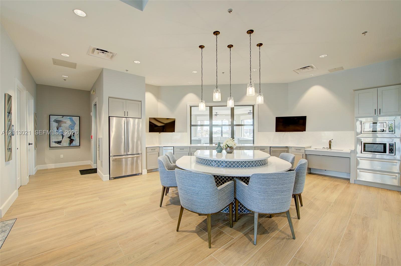 Kitchen featuring wood-finish flooring, stainless steel appliances, built-in wall ovens, and a circular island with stone-finish countertops and decorative tile detailing