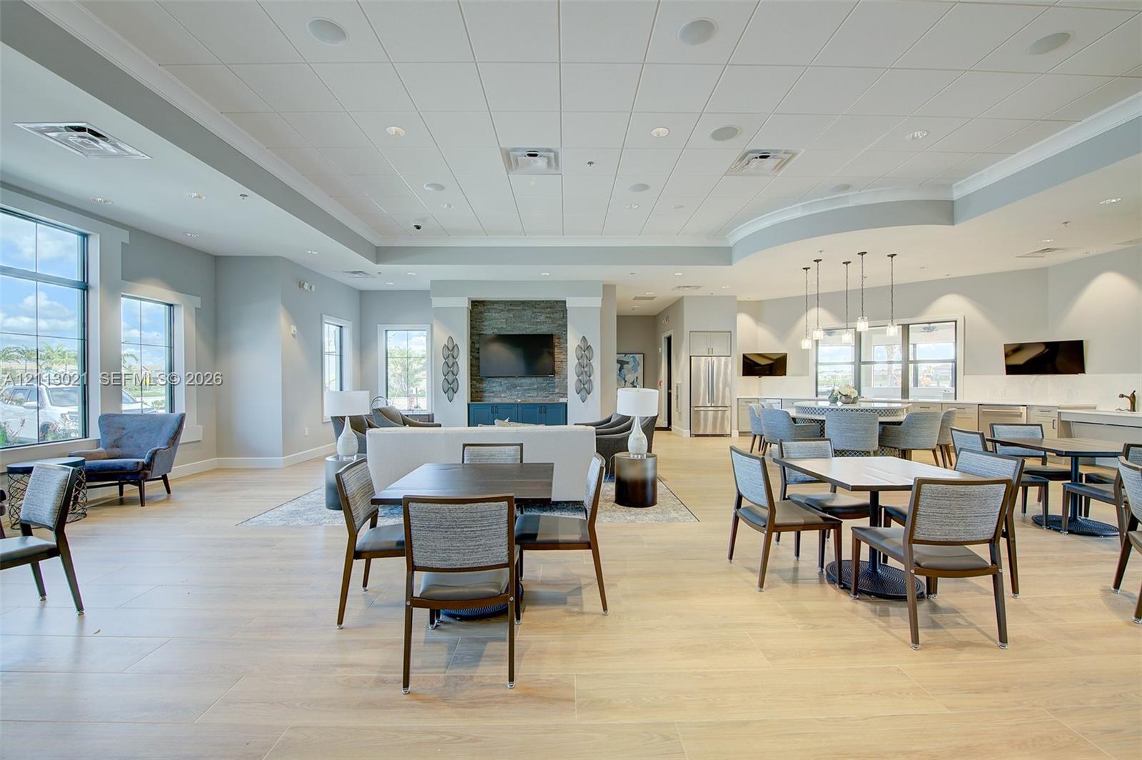 Open-concept common area featuring wood-finish flooring, tray ceiling with recessed lighting, stone-accented wall with built-in media cabinet, and a kitchenette with stainless steel appliances