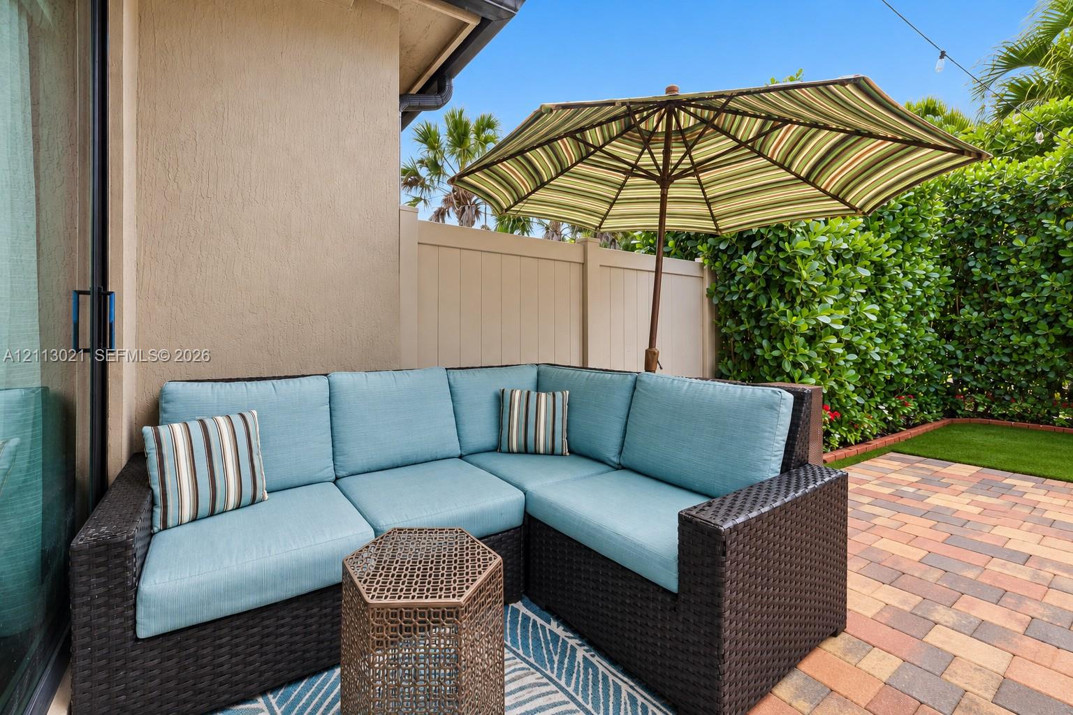 Private outdoor patio featuring multi-tone paver flooring, synthetic turf, and a solid perimeter privacy fence with mature shrubbery