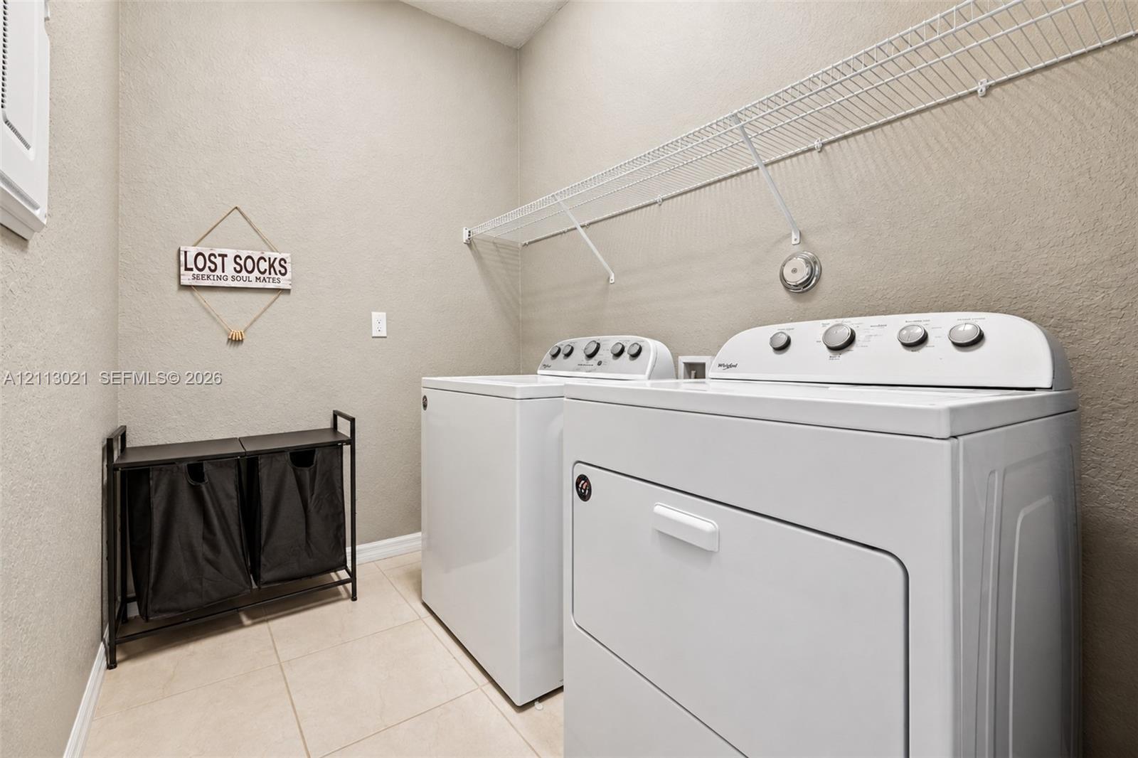 Laundry area featuring neutral-toned tile flooring, textured wall finishes, and integrated white wire shelving