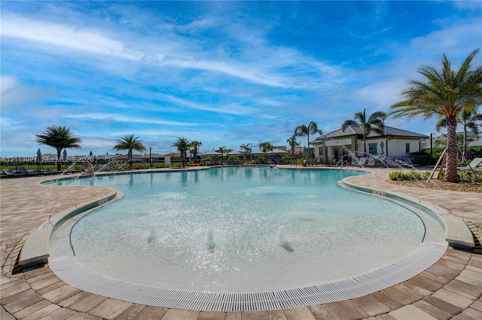 Swimming pool featuring a beach-entry slope, integrated water fountain jets, and paver stone hardscaping surrounded by mature palm trees
