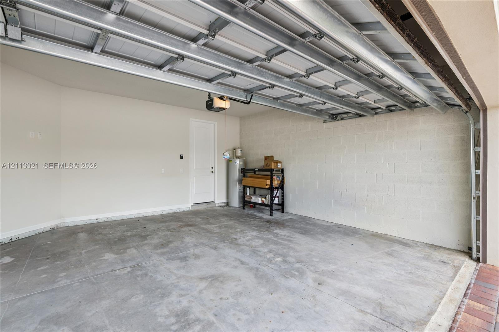 Two-car garage featuring finished concrete flooring, masonry block walls, an automatic overhead door opener, and an integrated water heater