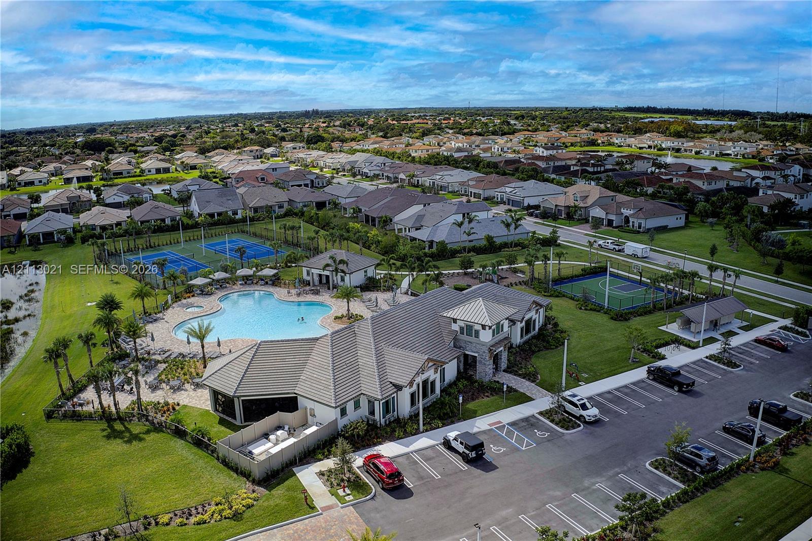 Community clubhouse facility featuring a swimming pool, tennis courts, basketball court, and paved parking area