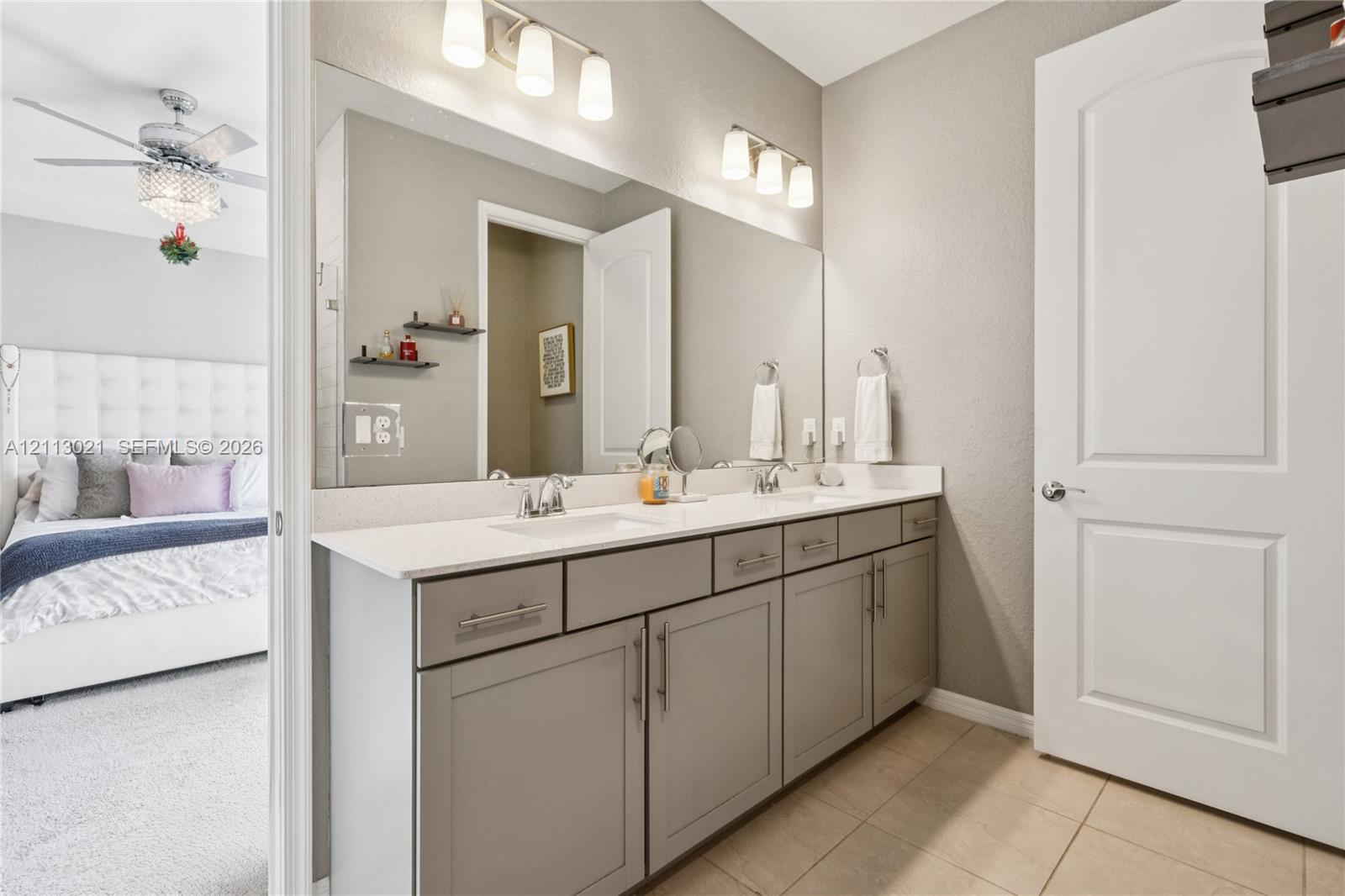 Dual-sink vanity with a solid surface countertop, shaker-style cabinetry, two wall-mounted light fixtures, and a large-format mirror