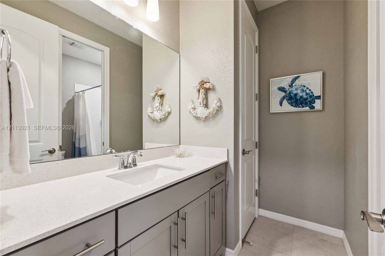 Vanity featuring a stone-composite countertop, undermount sink, and shaker-style cabinetry with polished metal hardware, complemented by a large wall-mounted mirror and integrated lighting
