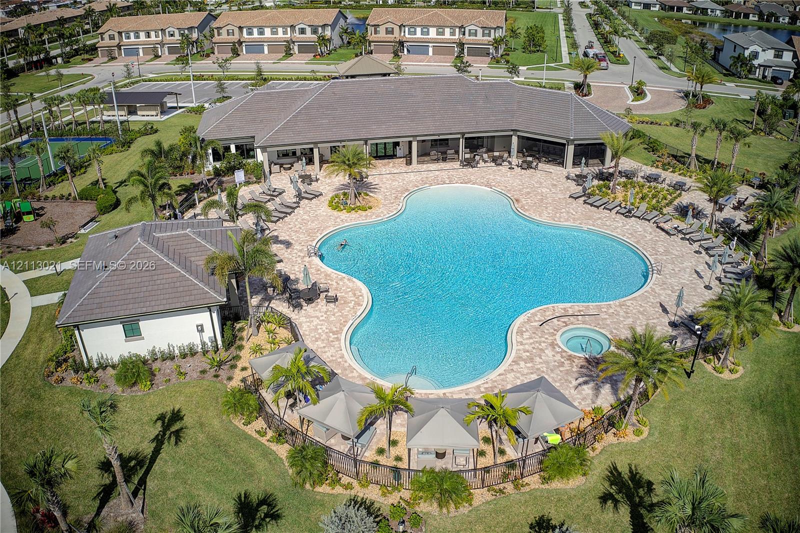 Community clubhouse featuring a large swimming pool, an integrated spa, paver pool deck, and shaded cabanas surrounded by landscaped grounds