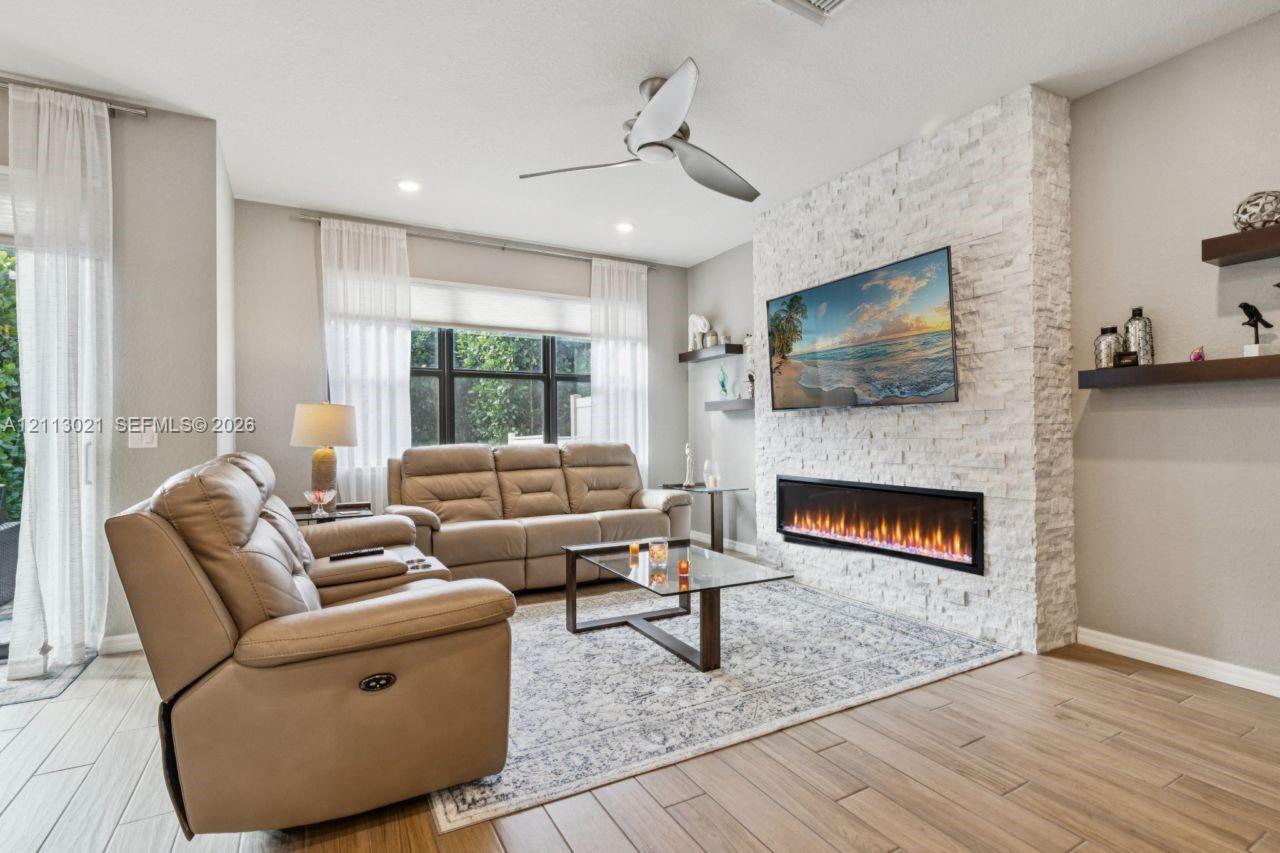 Living area featuring a floor-to-ceiling white stone fireplace surround, modern linear electric fireplace, wood-finish flooring, recessed lighting, and floating wall shelves Living area featuring a floor-to-ceiling white stone fireplace surround, modern linear electric fireplace, wood-finish flooring, recessed lighting, and floating wall shelves