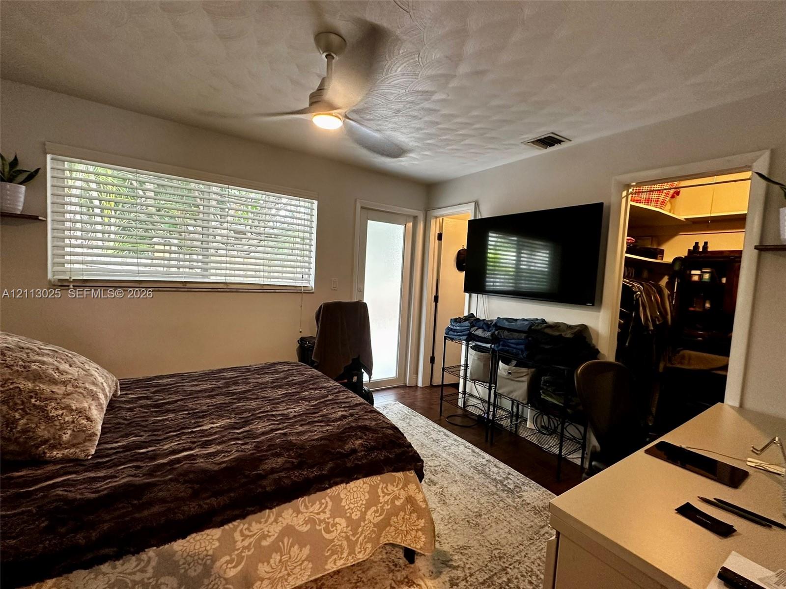 Textured ceiling, ceiling fan with integrated lighting, wood-finish flooring, horizontal blinds, and a walk-in closet