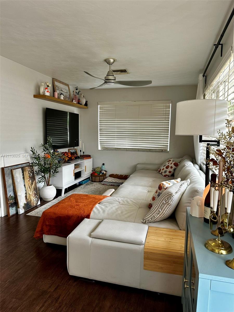Wood-finish flooring, floating wall-mounted shelving, ceiling fan with integrated lighting, and horizontal window blinds