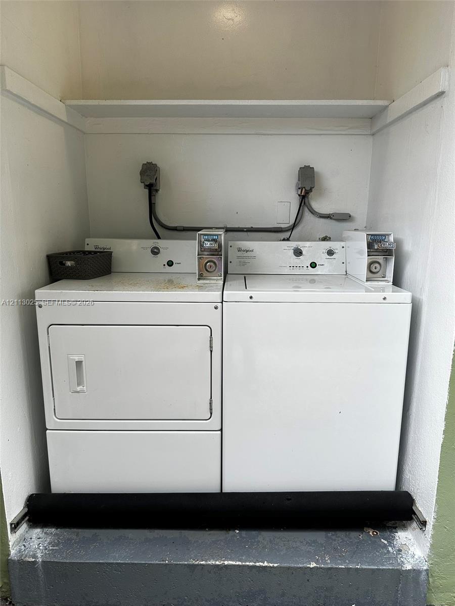 Laundry area featuring a side-by-side coin-operated washer and dryer set with an overhead built-in storage shelf