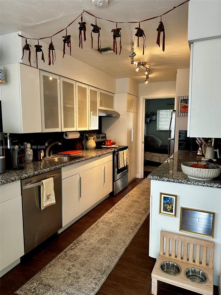 Kitchen featuring white cabinetry with frosted glass inserts, speckled stone countertops, stainless steel appliances, and dark wood-finish flooring