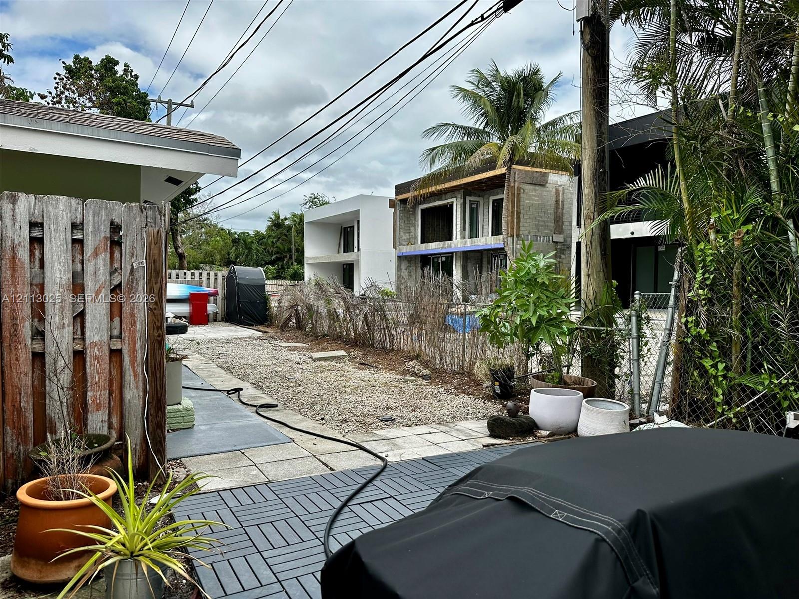 Outdoor space featuring a gray modular tile patio, gravel ground cover, vertical wood-plank fencing, and mature palm trees