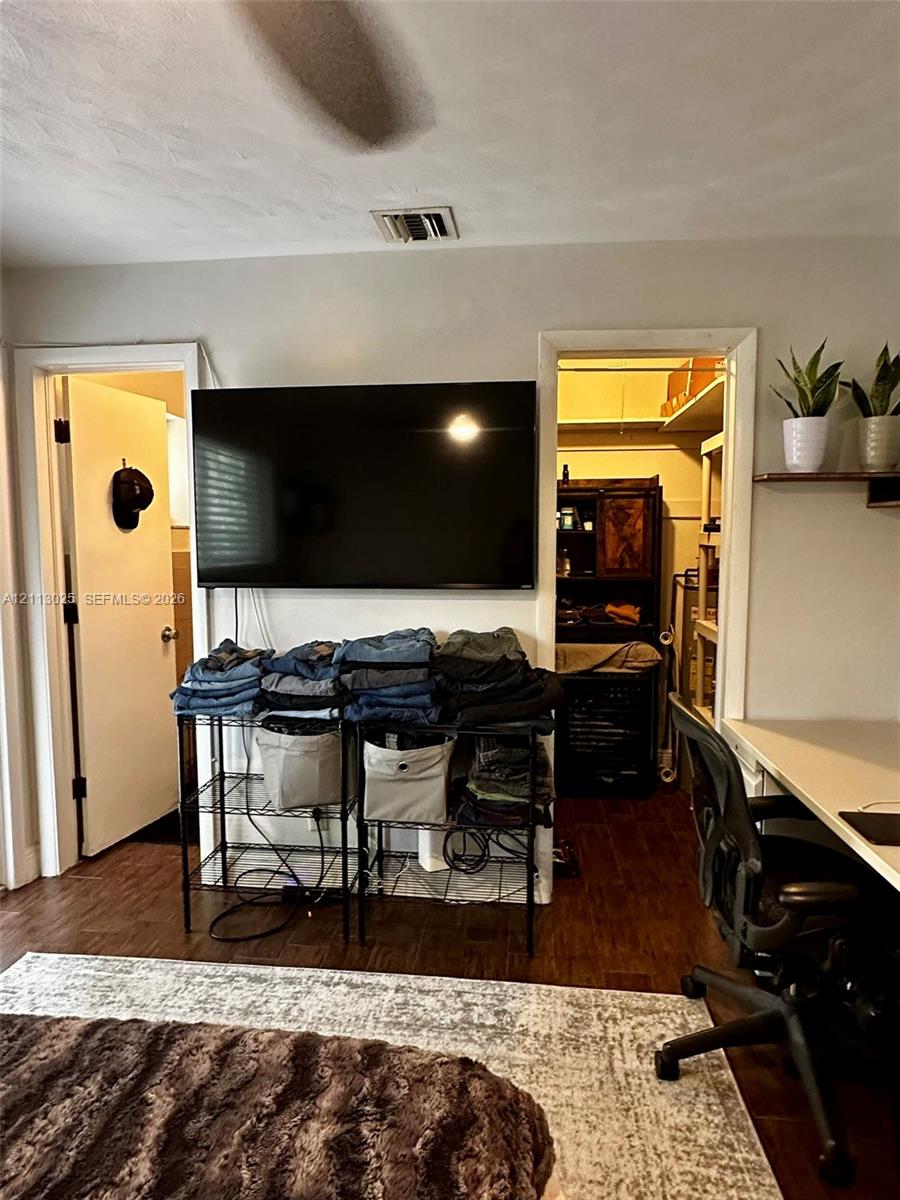 Room featuring dark wood-finish flooring, a built-in wall desk, and a walk-in closet with integrated shelving