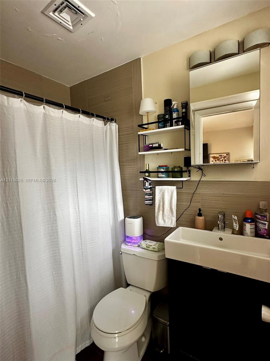 Bathroom featuring horizontal wall tiling, a wall-mounted medicine cabinet with a mirror, a rectangular vessel sink, and a black vanity base