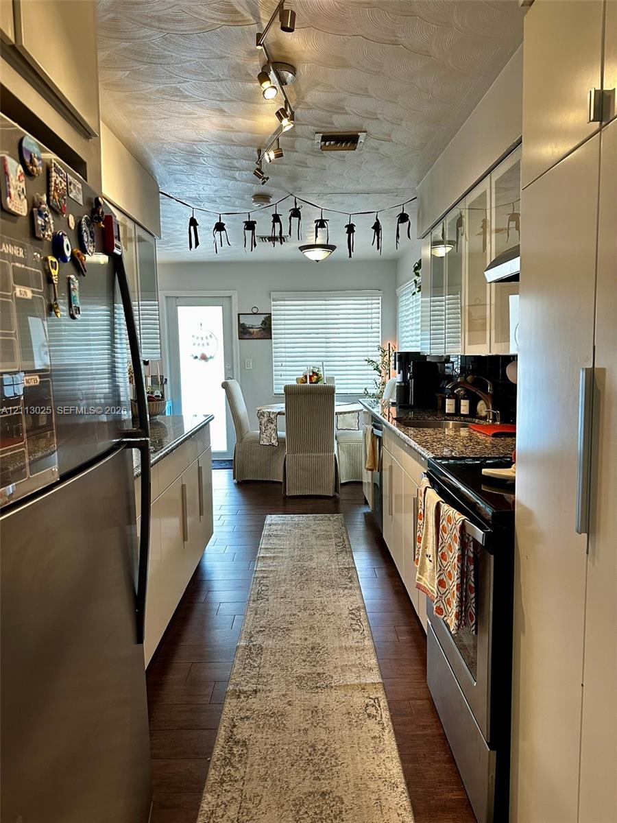 Galley kitchen featuring flat-panel cabinetry, stone countertops, stainless steel appliances, wood-finish flooring, and multi-directional track lighting