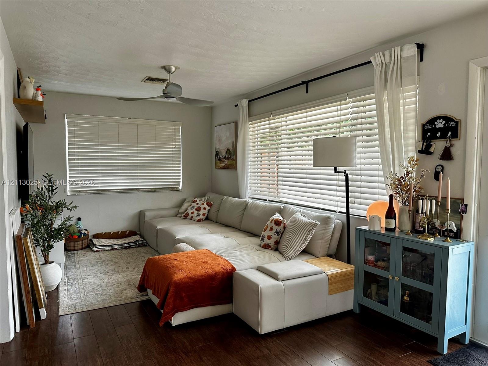 Living area featuring wood-finish flooring, a ceiling fan, and large windows with horizontal blinds
