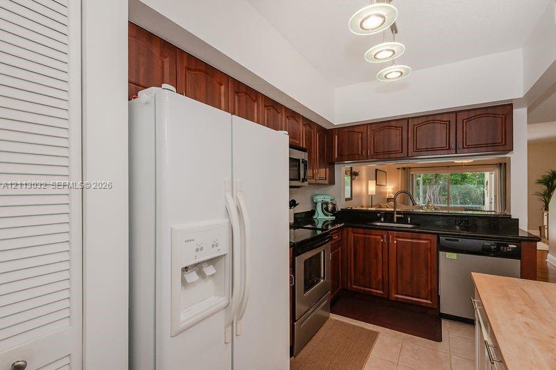 Kitchen featuring dark wood-finish cabinetry, black stone countertops, stainless steel appliances, tile flooring, and a three-light pendant fixture