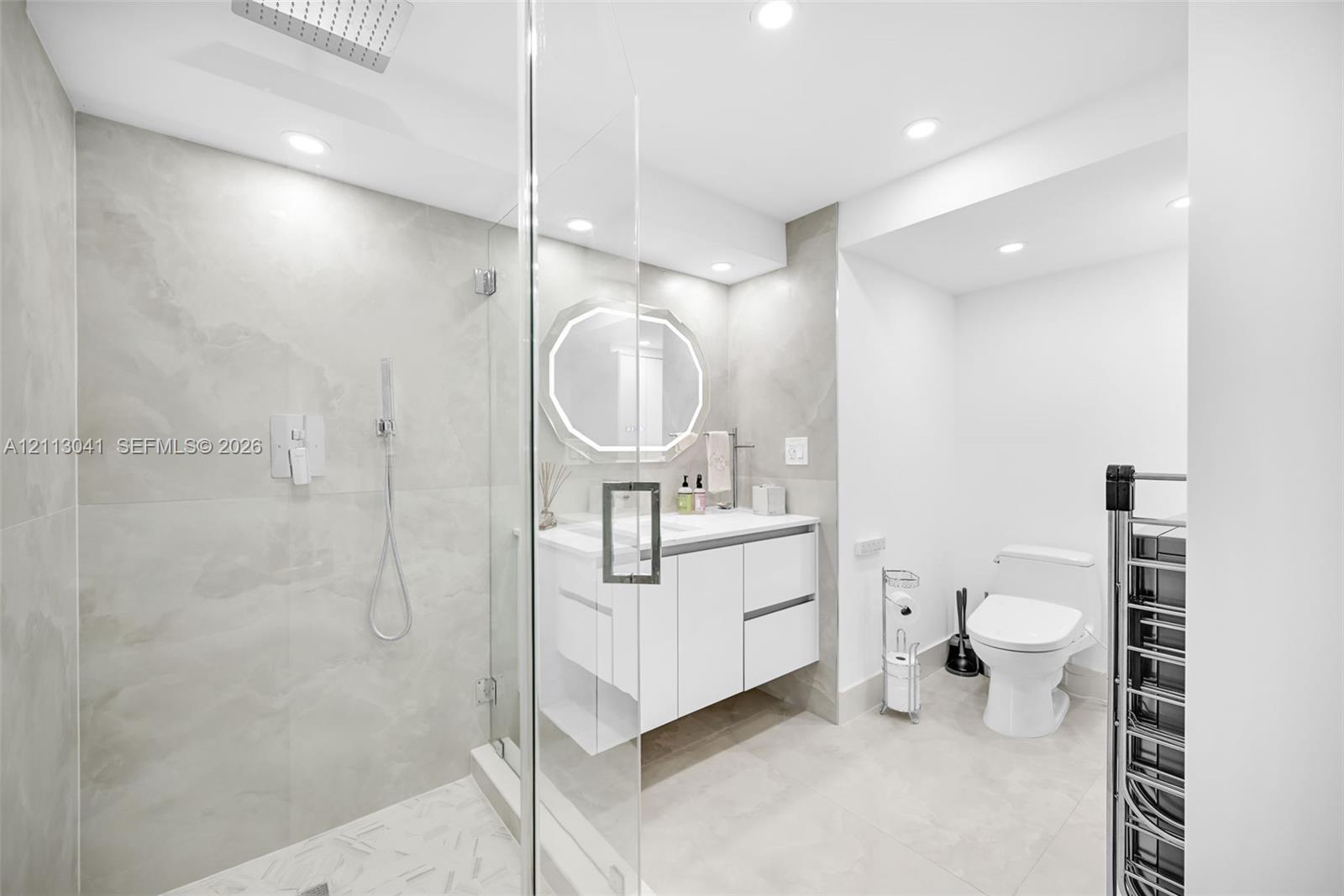 Walk-in shower with floor-to-ceiling stone-finish tile, rainfall shower head, glass enclosure, floating vanity, and recessed lighting