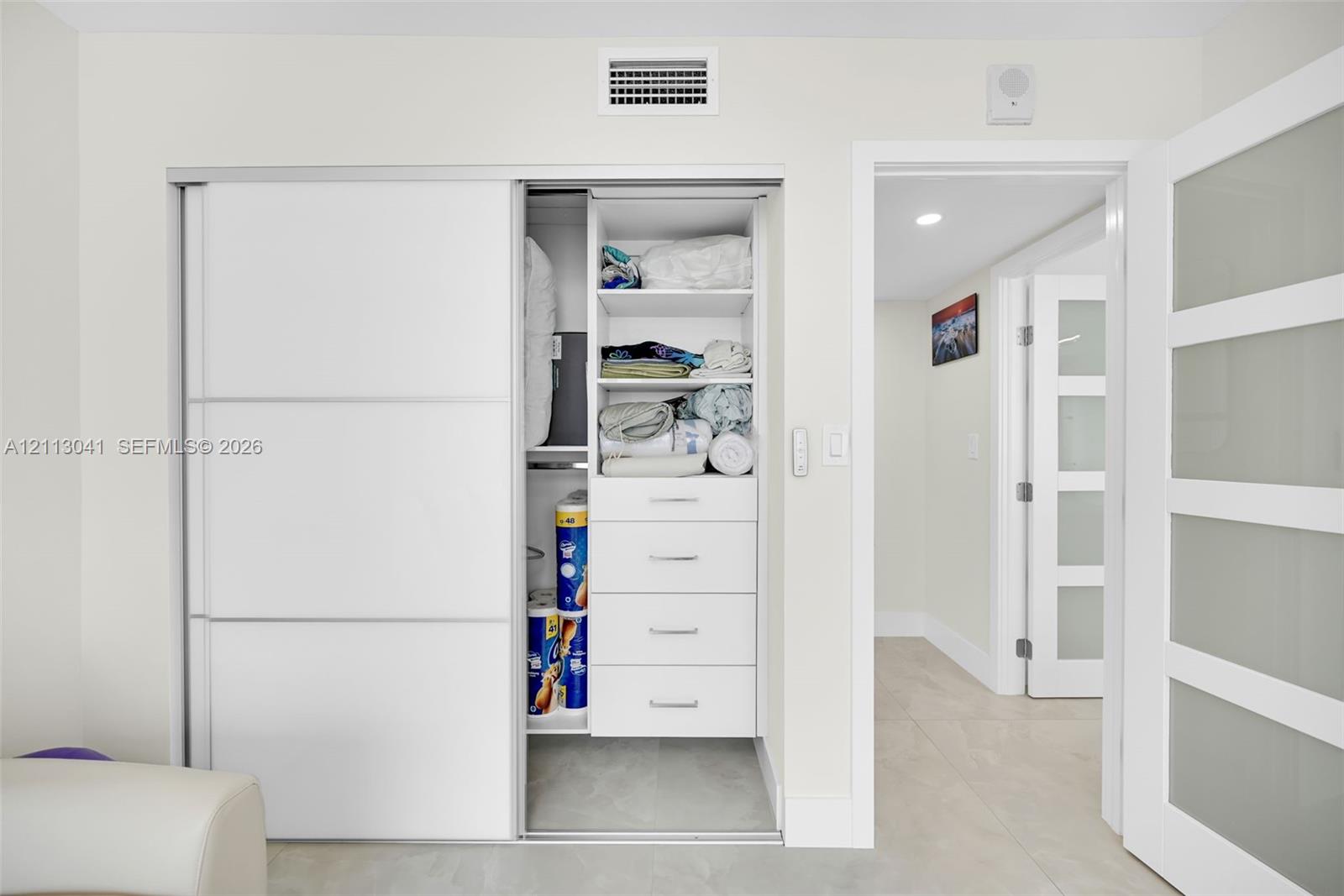 Storage closet featuring white sliding doors, built-in shelving, and integrated drawers, with paneled doors with frosted glass inserts