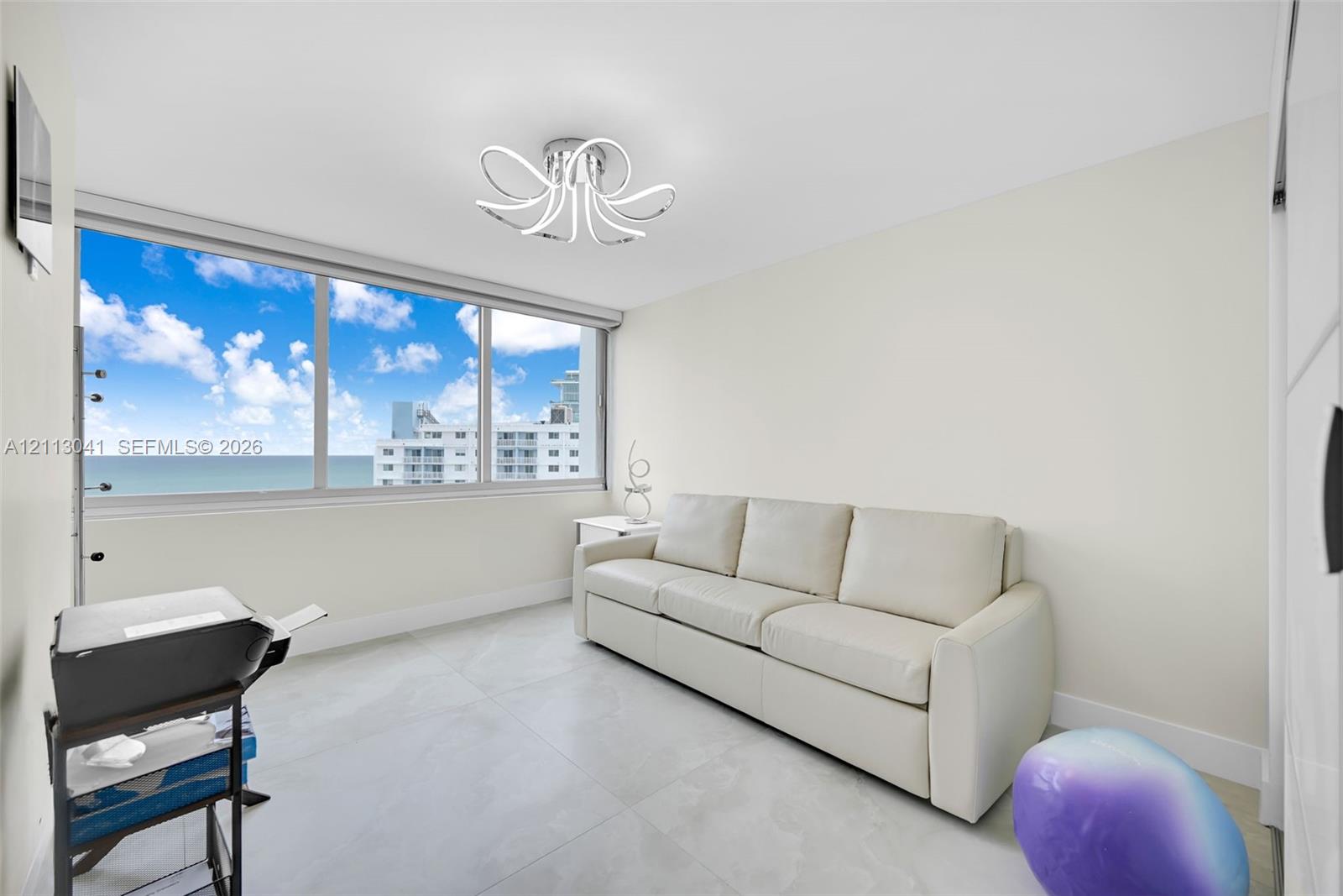 Large-format window featuring expansive coastal scenery, oversized light-colored floor tiles, and a contemporary multi-arm LED light fixture
