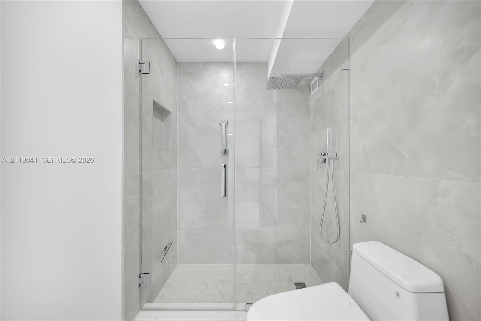 Walk-in shower featuring a frameless glass enclosure, floor-to-ceiling large-format tile surround, integrated shower niche, and wall-mounted shower system