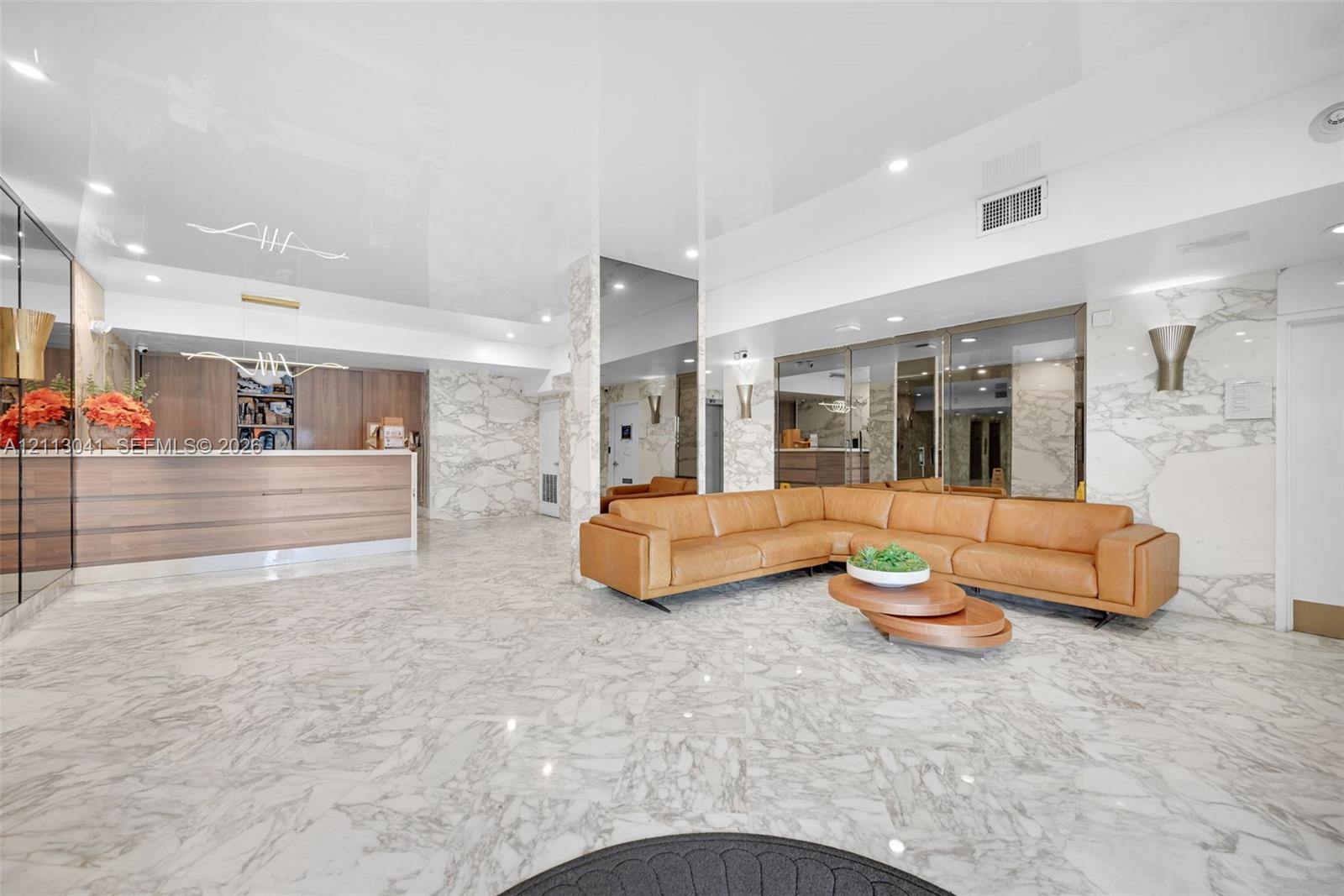 Lobby featuring large-format stone flooring, floor-to-ceiling mirrored walls, stone-clad accent pillars, integrated recessed lighting, and built-in wood-finish reception cabinetry