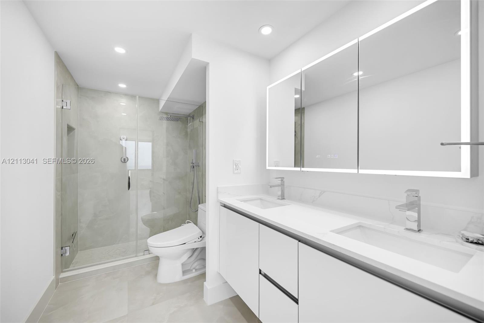 Bathroom featuring a floating double vanity with a stone countertop, integrated LED-lit medicine cabinets, a glass-enclosed walk-in shower with a rainfall showerhead, and tile flooring