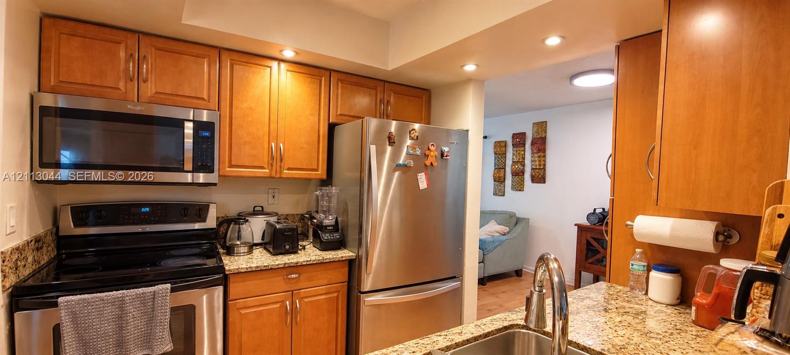 Kitchen featuring stone-finish countertops, stainless steel appliances, custom wood-finish cabinetry, and recessed lighting
