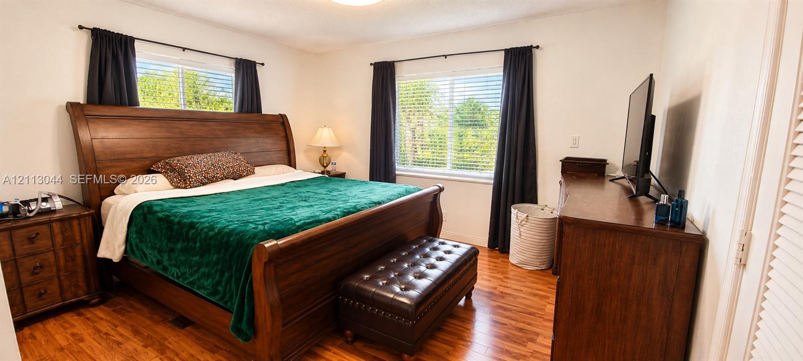 Bedroom featuring wood-finish flooring, dual windows with horizontal blinds, and louvered closet doors