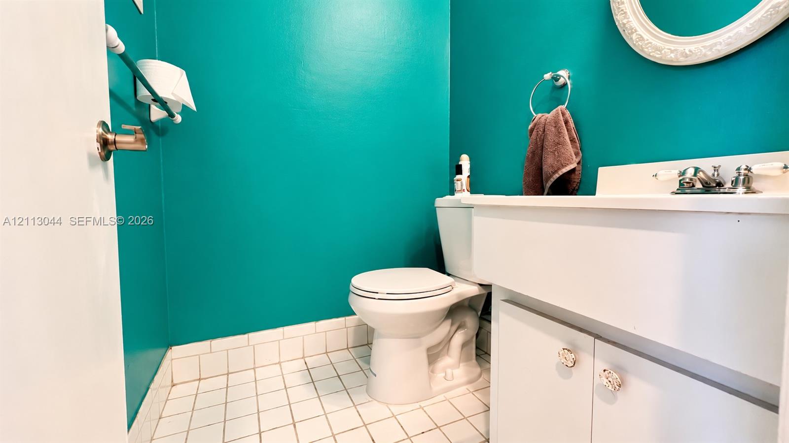 Bathroom featuring white cabinetry, an integrated sink with polished chrome hardware, a wall-mounted oval mirror, and tiled flooring