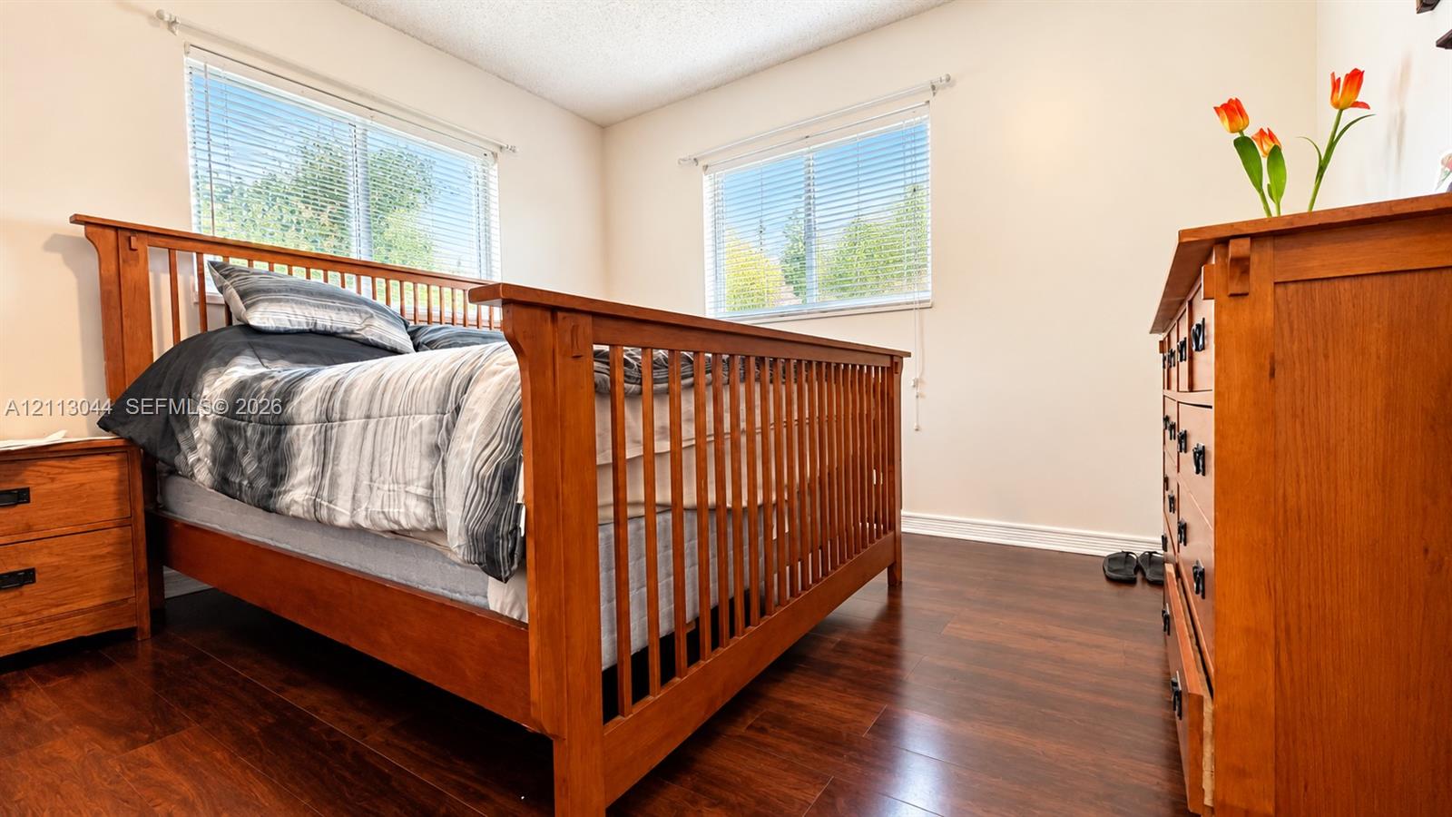 Room featuring dark wood-finish flooring and two windows with horizontal blinds