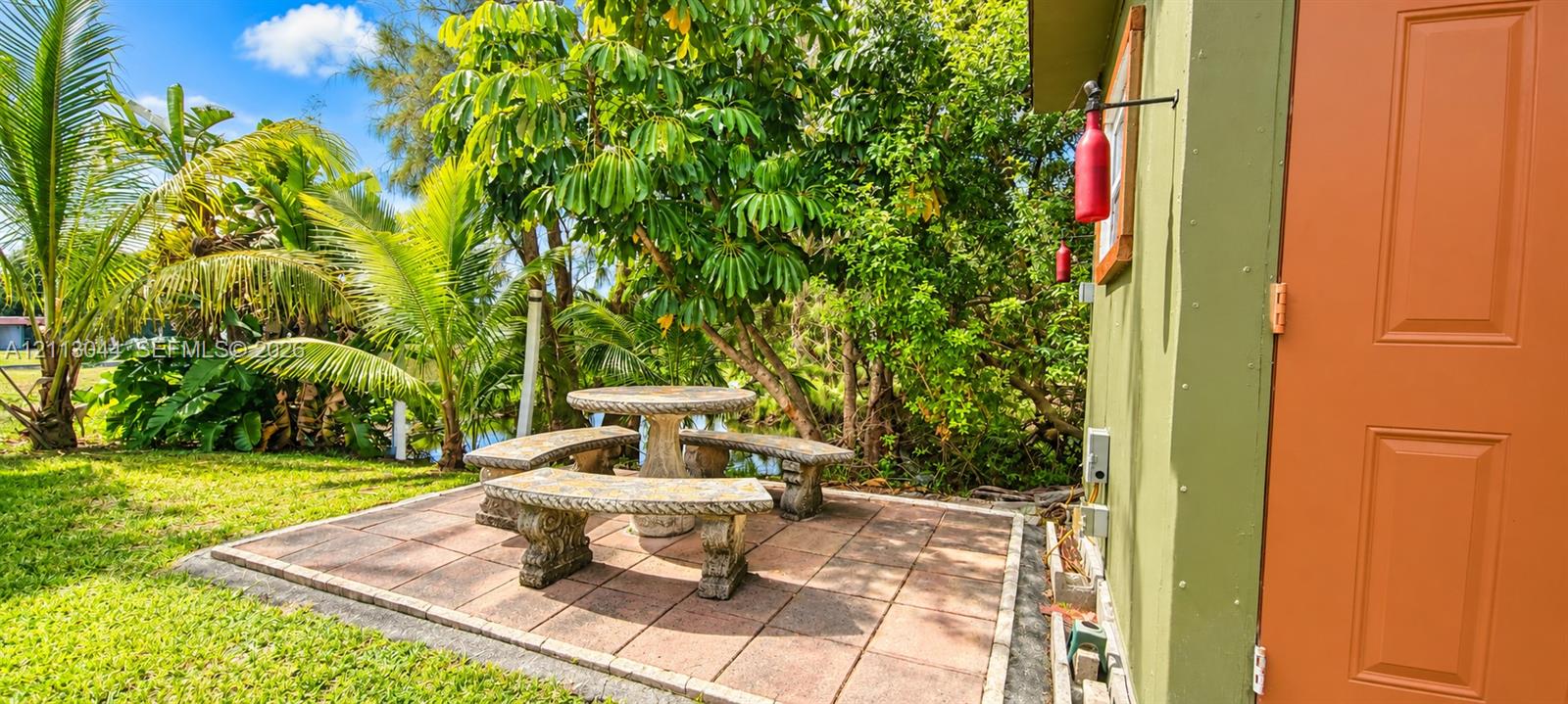 Outdoor stone paver patio featuring an integrated stone table and bench set, surrounded by established landscaping and palm trees
